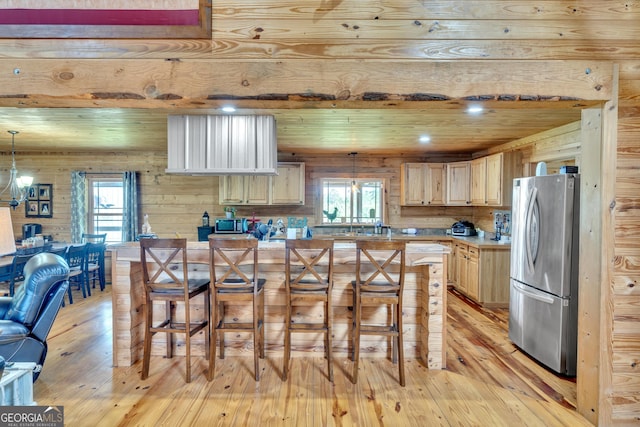 kitchen featuring a kitchen bar, hanging light fixtures, appliances with stainless steel finishes, and light hardwood / wood-style flooring