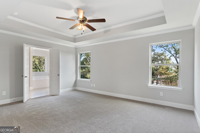 empty room with light colored carpet, ceiling fan, a raised ceiling, and a healthy amount of sunlight