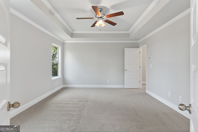 empty room featuring carpet floors, a raised ceiling, crown molding, and ceiling fan