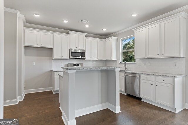 kitchen featuring appliances with stainless steel finishes, white cabinetry, light stone counters, dark hardwood / wood-style flooring, and a center island