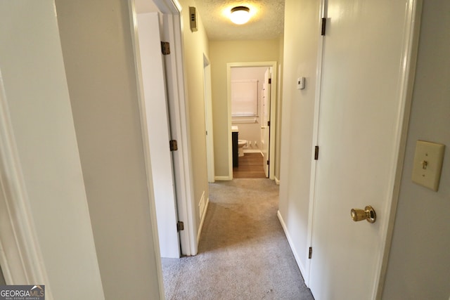 corridor with a textured ceiling and light colored carpet