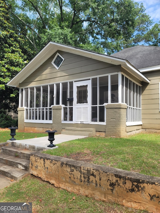 view of front of house featuring brick siding, a shingled roof, a front lawn, and a sunroom