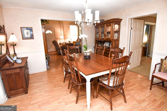 dining space with light wood-style flooring, a decorative wall, ornamental molding, and a chandelier