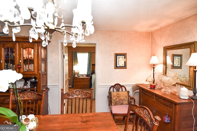 dining space with a notable chandelier, wainscoting, a textured ceiling, and ornamental molding