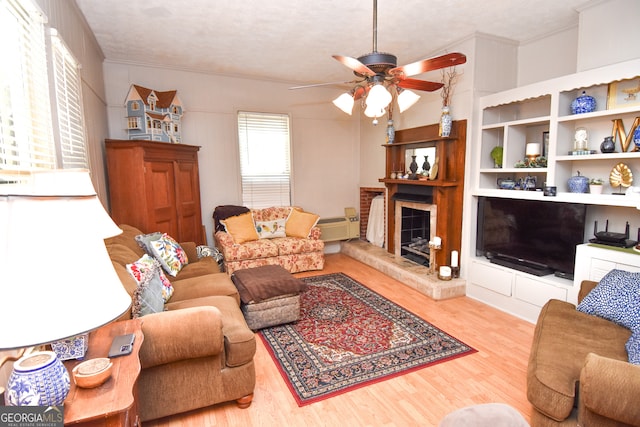 living room with a textured ceiling, ceiling fan, light hardwood / wood-style flooring, and a fireplace