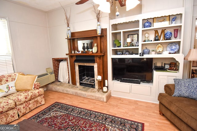 living room featuring a ceiling fan, wood finished floors, a wall mounted air conditioner, and a fireplace with raised hearth