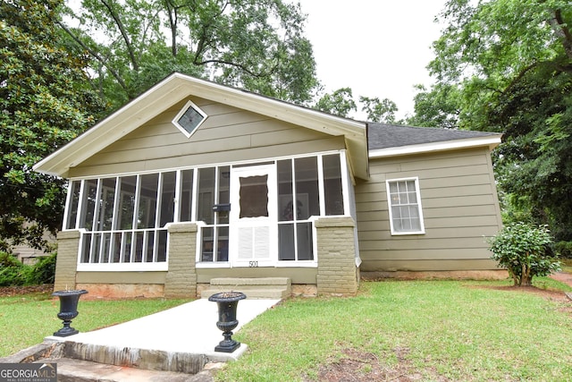 view of front of property with a front lawn, a sunroom, and roof with shingles