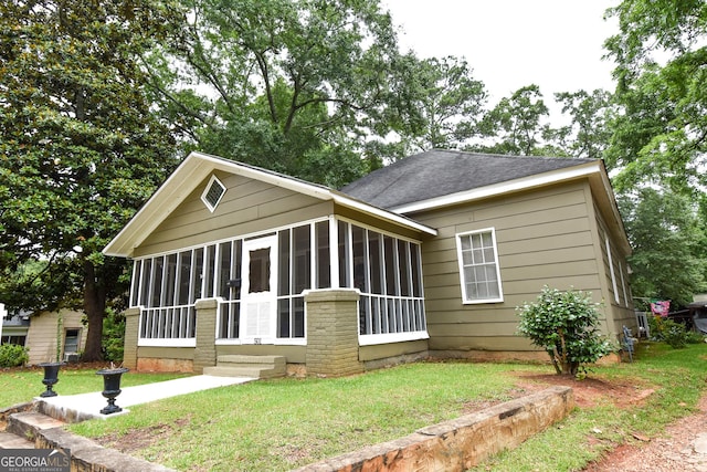 view of front of house with a front yard, a sunroom, and a shingled roof