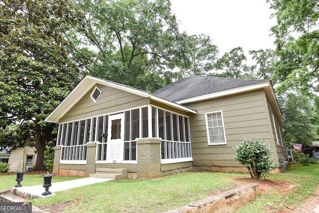 view of front facade with a shingled roof, a front yard, and a sunroom