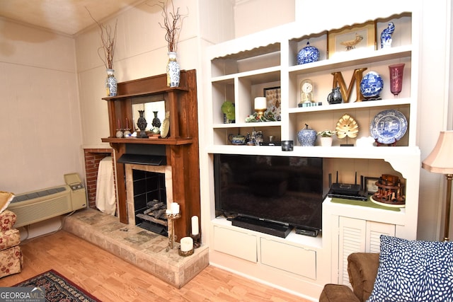 living area featuring wood finished floors, a wall mounted air conditioner, and a fireplace with raised hearth