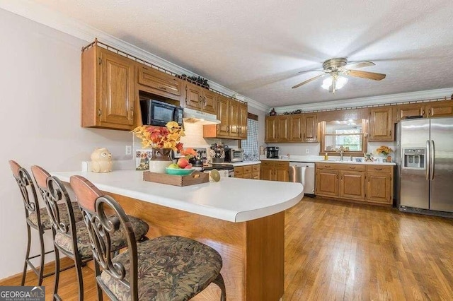 kitchen with sink, light hardwood / wood-style floors, kitchen peninsula, stainless steel appliances, and crown molding