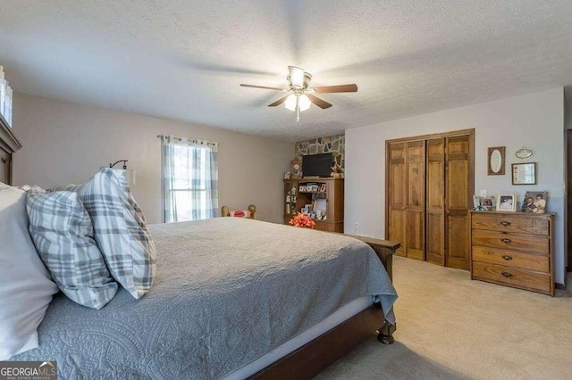 bedroom featuring ceiling fan, light colored carpet, a closet, and a textured ceiling