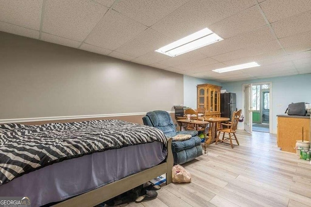 bedroom with black refrigerator, a paneled ceiling, and light hardwood / wood-style floors