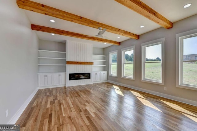 unfurnished living room with built in shelves, beamed ceiling, a large fireplace, and light hardwood / wood-style floors