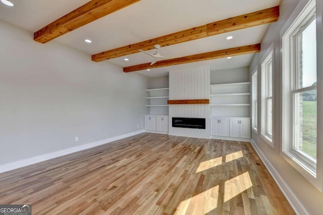 unfurnished living room with built in shelves, ceiling fan, beam ceiling, a fireplace, and light hardwood / wood-style flooring