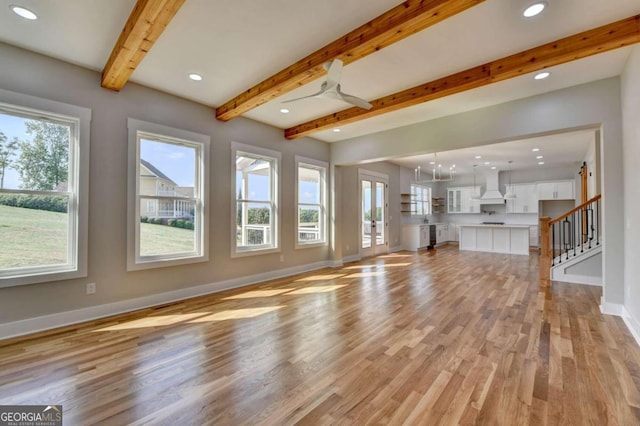 unfurnished living room with beamed ceiling, french doors, light hardwood / wood-style floors, and plenty of natural light