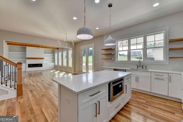 kitchen featuring stainless steel microwave, hanging light fixtures, sink, and white cabinets