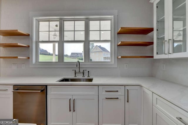 kitchen with light stone countertops, white cabinetry, sink, and stainless steel dishwasher