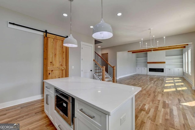 kitchen with a barn door, decorative light fixtures, white cabinets, stainless steel microwave, and light hardwood / wood-style flooring