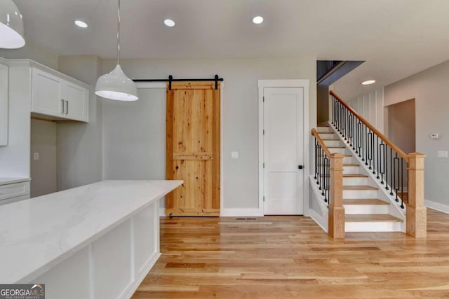 kitchen with white cabinetry, light stone counters, decorative light fixtures, a barn door, and light wood-type flooring