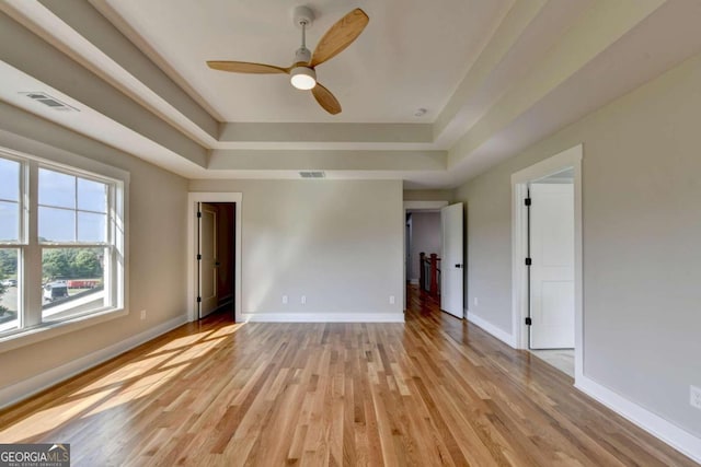 empty room featuring light hardwood / wood-style floors, ceiling fan, and a tray ceiling