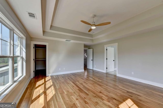 unfurnished room with light hardwood / wood-style floors, ceiling fan, and a raised ceiling