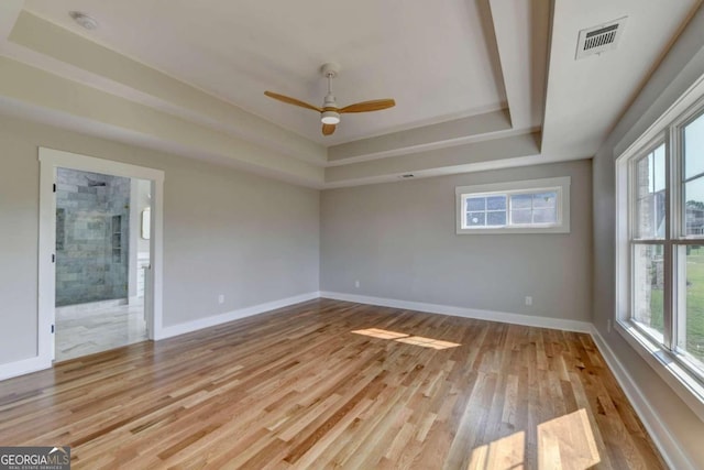 unfurnished room featuring a raised ceiling, ceiling fan, and light hardwood / wood-style flooring