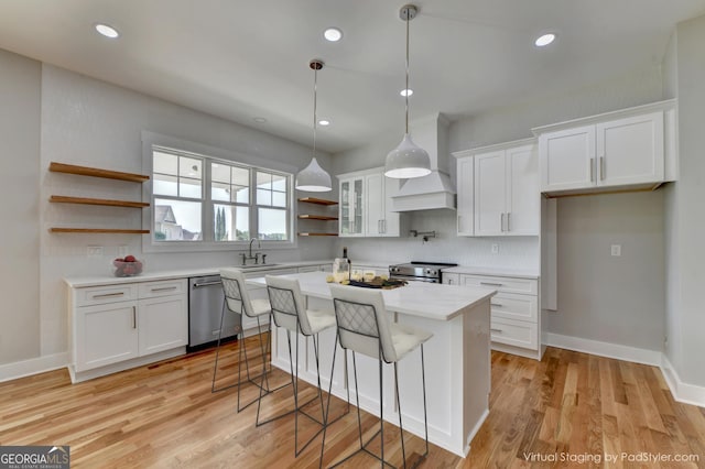 kitchen with appliances with stainless steel finishes, custom exhaust hood, light hardwood / wood-style flooring, a center island, and white cabinets