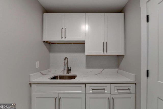 kitchen with sink, light stone counters, and white cabinets