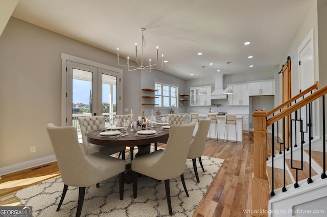 dining room with french doors, light wood-type flooring, a notable chandelier, and a barn door