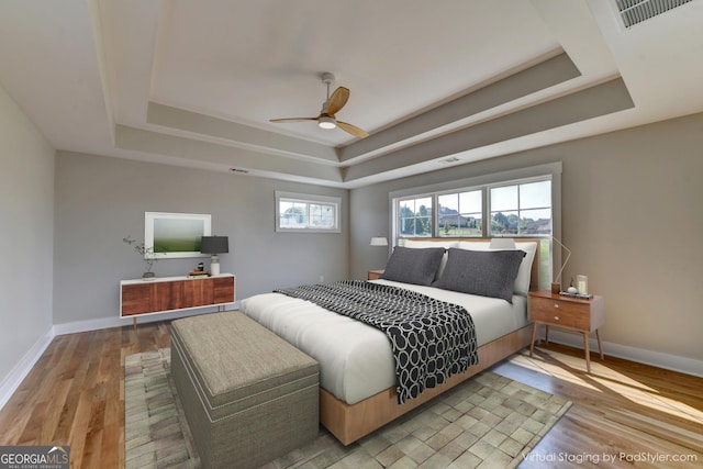 bedroom with light wood-type flooring, ceiling fan, and a tray ceiling