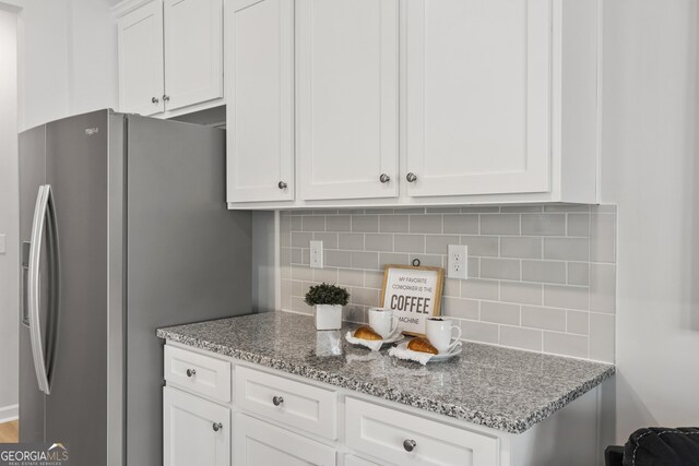 kitchen featuring decorative backsplash, stainless steel fridge, white cabinetry, and light stone countertops