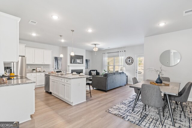 kitchen featuring white cabinetry, a center island with sink, decorative light fixtures, and appliances with stainless steel finishes