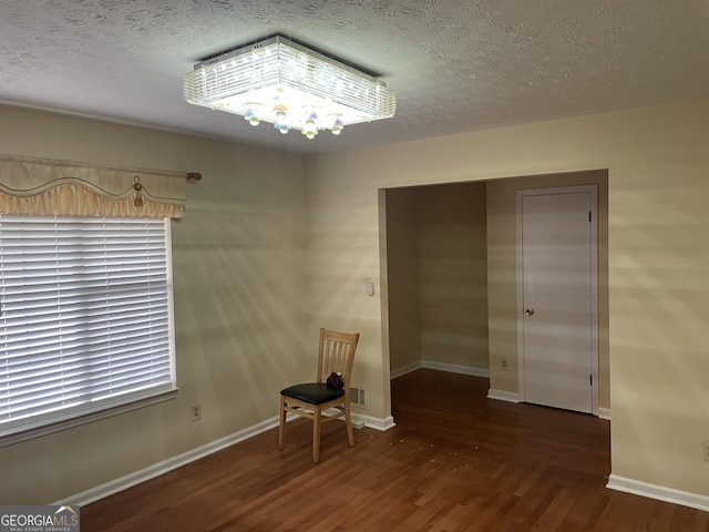 empty room with a chandelier, a textured ceiling, and dark hardwood / wood-style flooring