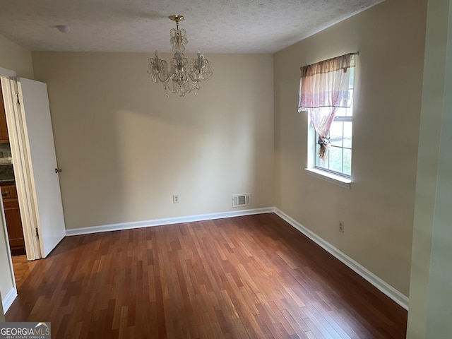 spare room featuring a textured ceiling, dark hardwood / wood-style flooring, and an inviting chandelier