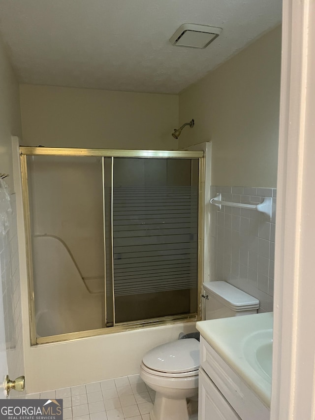 full bathroom featuring vanity, shower / bath combination with glass door, tile patterned floors, toilet, and tile walls