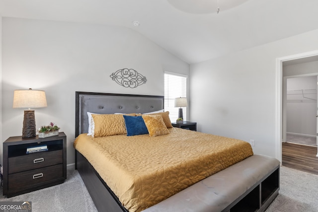 bedroom featuring a spacious closet, vaulted ceiling, light colored carpet, and a closet