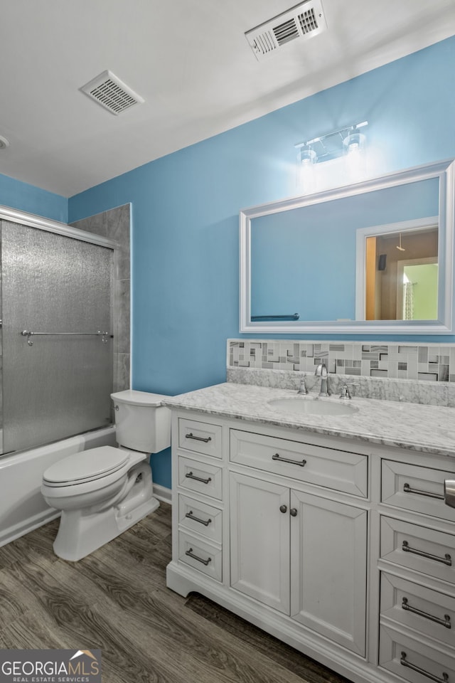 full bathroom featuring toilet, wood-type flooring, backsplash, vanity, and combined bath / shower with glass door