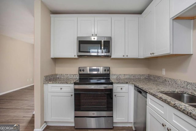 kitchen featuring white cabinetry, light stone counters, hardwood / wood-style flooring, and appliances with stainless steel finishes