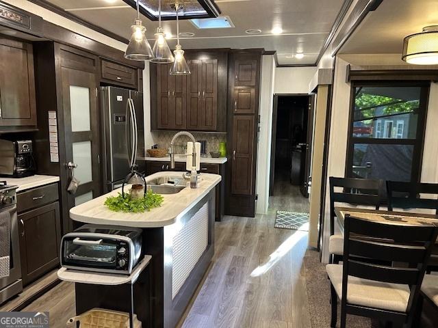 kitchen with stainless steel refrigerator with ice dispenser, ornamental molding, dark brown cabinetry, sink, and a center island with sink