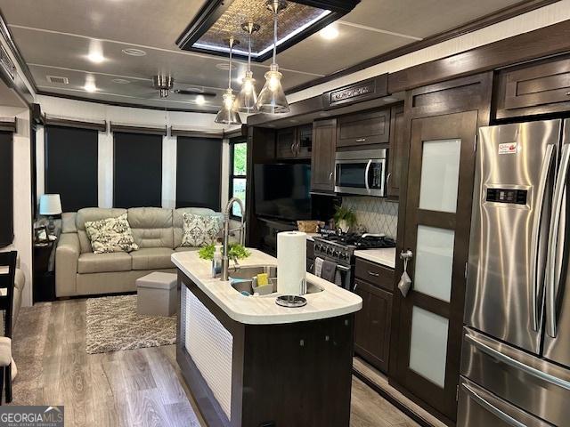 kitchen with pendant lighting, dark wood-type flooring, sink, an island with sink, and appliances with stainless steel finishes