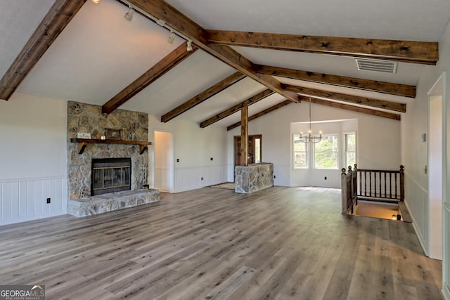 unfurnished living room with rail lighting, a fireplace, lofted ceiling with beams, a chandelier, and light wood-type flooring