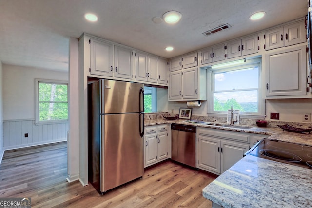 kitchen featuring sink, light hardwood / wood-style flooring, appliances with stainless steel finishes, white cabinetry, and light stone counters