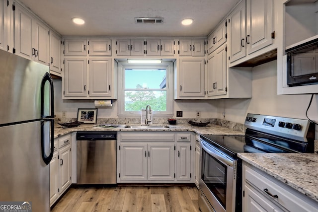 kitchen featuring white cabinetry, sink, light hardwood / wood-style floors, stainless steel appliances, and light stone countertops