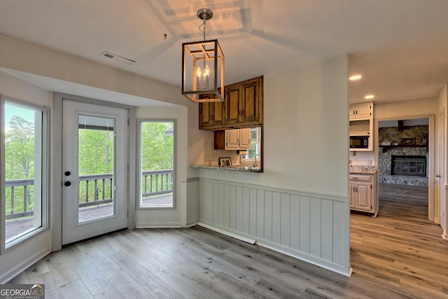 kitchen with light stone countertops, a stone fireplace, pendant lighting, and light wood-type flooring