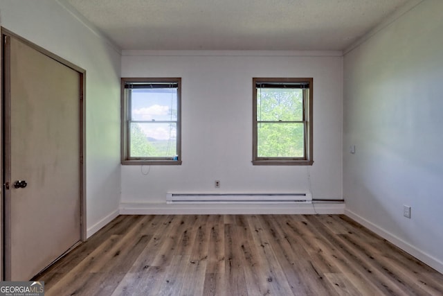 empty room with baseboard heating, ornamental molding, a textured ceiling, and hardwood / wood-style flooring