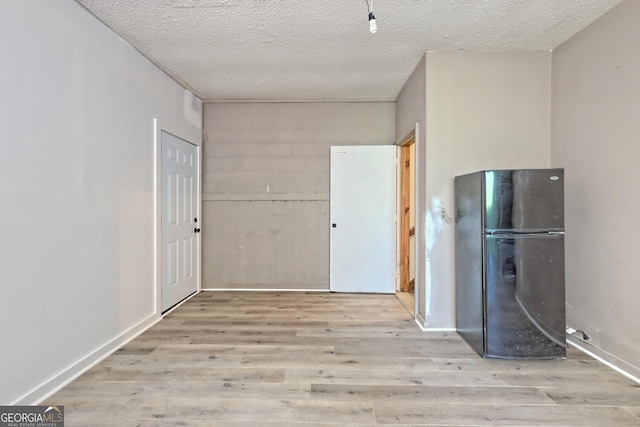 kitchen with black refrigerator, a textured ceiling, and light wood-type flooring