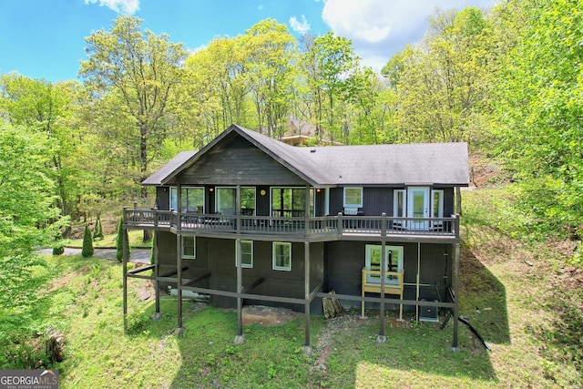 back of property with a sunroom, a deck, and a lawn