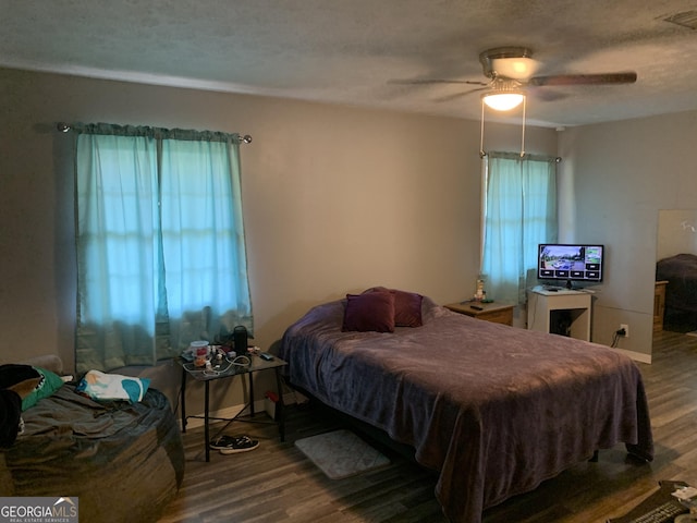 bedroom featuring ceiling fan, wood-type flooring, a textured ceiling, and multiple windows