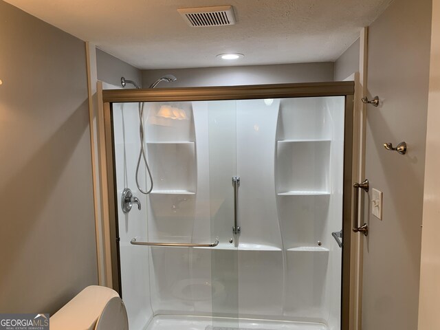 bathroom with toilet, a textured ceiling, and walk in shower